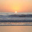 Closeup square photo of a setting sun in an ocean reflecting an orange sky.