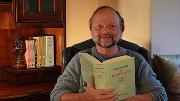 Photo of Martin Janello, author of Philosophy of Happiness, seated at his desk, reading from the book.