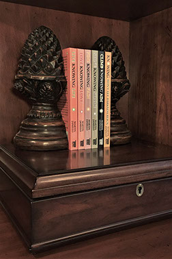 Photo of all 6 in print books of the Knowing series authored by Martin Janello on a wooden bookshelf.