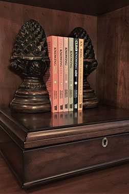 Photo of all 6 in print books of the Knowing series authored by Martin Janello on a wooden bookshelf.